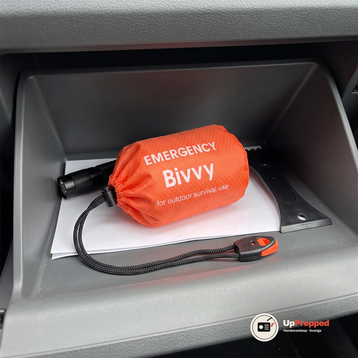 Öppet handskfack med den orange förvaringspåsen och visselpipan, en ficklampa, en isskrapa och ett vitt papper