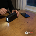 Händer vevar den svarta nödradion på ett köksbord, en mobil med kabel ligger bredvid