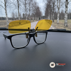 Svarta glasögon med uppfällda gula clip-on linser på instrumentbrädan i en bil