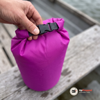 Närbild på spännet och den hoprullade toppen på en lila drybag med vattendroppar på sittbrädan i en roddbåt