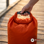 Hand som håller i öglan och spännet på en orange drybag på en brygga i kvällsljus