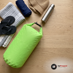 Grön drybag på sidan på ett bord med badlakan, badkläder, flip-flops, solhatt och termos