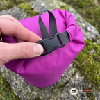 Närbild på spännet och den hoprullade toppen på en lila drybag med vattendroppar