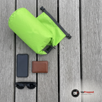 Grön drybag på bryggplankor med mobil, plånbok och solglasögon som exempel på vad som ryms, endast påsen ingår