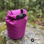 Närbild på spännet och den hoprullade toppen på en lila drybag med vattendroppar på en mossig granithäll