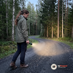 Kvinna går på en grusväg i skogen med tänd ficklampa riktad mot vägen
