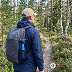 Vandrare sedd bakifrån med den blå vattenflaskan i ryggsäckens sidficka på en stig i skogen