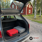 Slutet första hjälpen-kit i bagageutrymmet på en grå kombi på en grusuppfart vid ett rött trähus