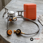 Gasbrännare med slang, adapter och orange förvaringsbox på ett grått träbord