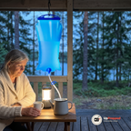 Kvinna i krämfärgad kofta sitter vid ett bord på en veranda i skymningen med en lykta medan vatten rinner från den hängda vattensäckens slang ner i en emaljkanna