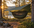 Hängmatta med regnskydd och myggnät uppsatt mellan träd i skogen vid solnedgång