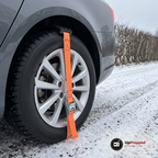 Hjulbrodd med orange rem och spänne fastspänd över däcket på en bil på en snöig grusväg