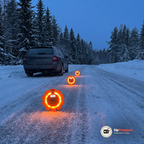 Tre orange LED varningsljus står på en snöig landsväg bakom en bil i skymningen