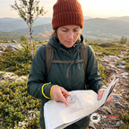 Kvinna lägger kartkompassen på en papperskarta på en bergsrygg i kvällssol