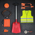 Nödpaketets alla delar uppifrån på ett mörkgrått bagagegolv: varningsljus, pannlampa, nödsovsäck, fönsterkross, snöskyffel, reflexväst och två hjulbroddar