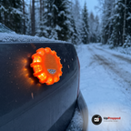 Orange LED varningsljus med magnet fäst på bagageluckan på en bil i skymningen med snöfall