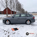 Kombi på en snöig gårdsväg med hjulbroddar fastspända på två hjul och två hjulbroddar utlagda på snön nedanför bilen