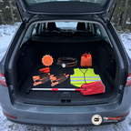 Nödpaketets delar utlagda i det öppna bagageutrymmet på en kombi vid en snöig skogsväg