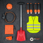 Nödpaketets alla delar uppifrån på ett mörkgrått bagagegolv: varningsljus, pannlampa, nödsovsäck, fönsterkross, snöskyffel, reflexväst och fyra hjulbroddar