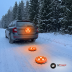 Tre orange LED varningsljus lyser, ett fäst på bagageluckan och två på den snöiga vägen bakom en kombi i skymningen