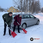 Man och kvinna skyfflar snö vid bakhjulet på en kombi med varsin röd teleskopisk snöskyffel