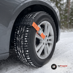 Hjulbrodd med orange rem och spänne fastspänd över däcket på en bil på en snöig grusväg