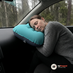 En kvinna sover i passagerarsätet i en bil med kinden mot campingkudden mellan huvudet och sidorutan