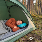 En kvinna sover på sidan i ett grönt tält med huvudet på den turkosa campingkudden
