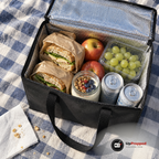Öppen kylbag 18 liter med silverfolie inuti, fylld med mackor, yoghurt, frukt och två kalla burkar på en picknickfilt