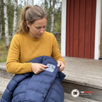 Kvinna trycker fast en genomskinlig reparationslapp på en mörkblå dunjacka på en stugtrappa