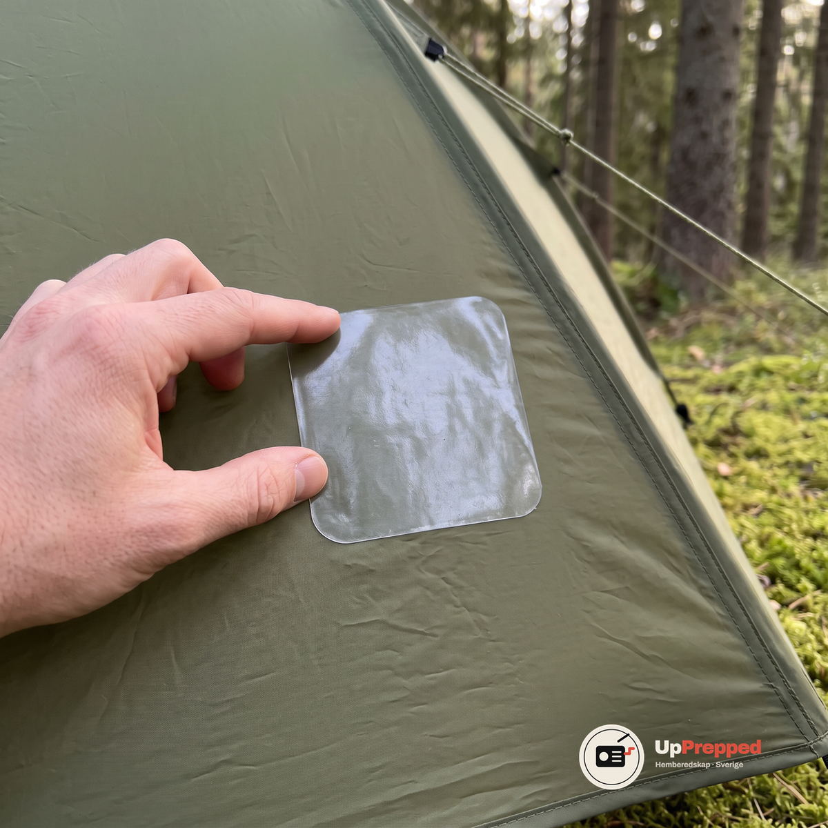 Hand trycker mot en genomskinlig reparationslapp på väggen av ett olivgrönt kupoltält i skogen