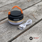 LED campinglampa och en vit USB-laddkabel på ett grått träbord