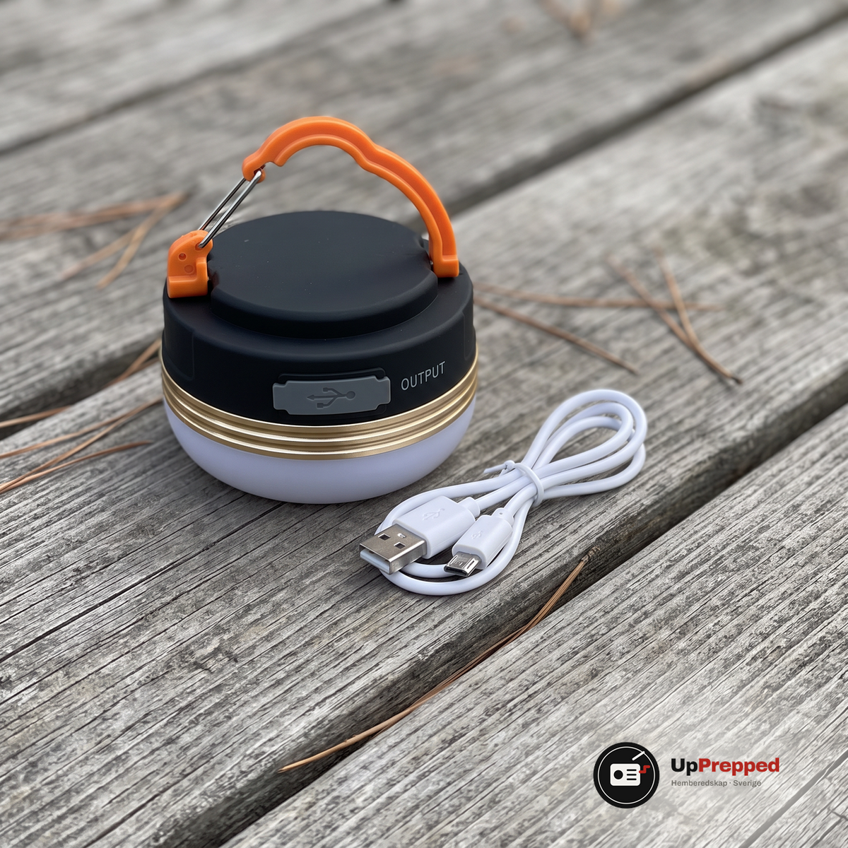 LED campinglampa och en vit USB-laddkabel på ett grått träbord