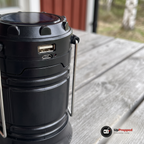 Närbild på lyktans övre ring med solcell, USB-uttag, mikro-USB-uttag och röd indikator på ett grått trädbord på en veranda