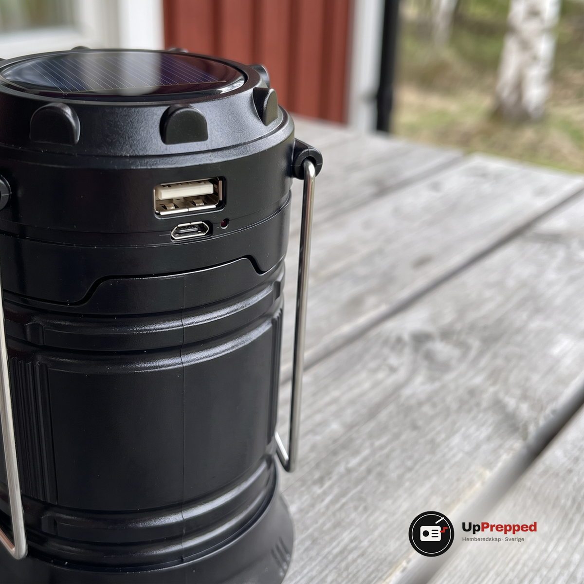 Närbild på lyktans övre ring med solcell, USB-uttag, mikro-USB-uttag och röd indikator på ett grått trädbord på en veranda