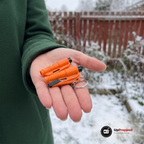 Två orange bältesskärare med glaskross och nyckelringar i en öppen handflata framför ett frostigt trädgårdsstaket