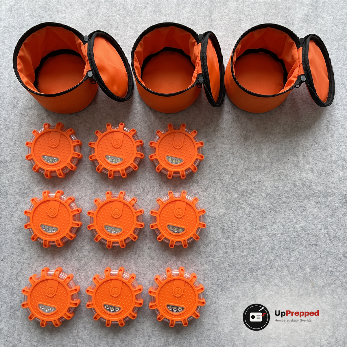 Det som ingår i nödpaketet uppifrån, del 2: tre öppna tomma förvaringsväskor och nio orange LED varningsljus i tre rader om tre på en grå filtmatta