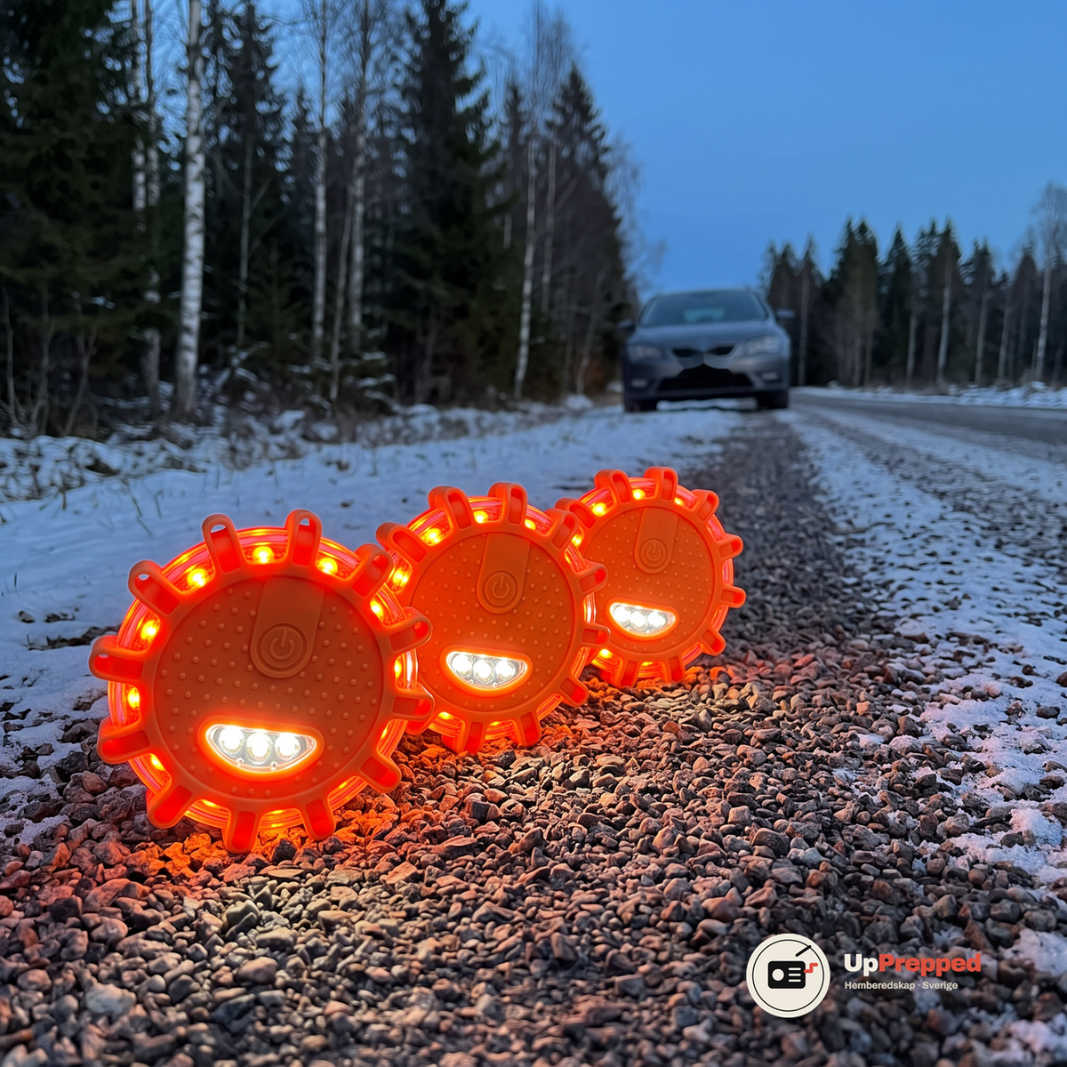 Tre orange LED varningsljus i rad med lysande röd-orange och vita lysdioder på en snöpudrad grusaxel vid en skogsväg i skymningen