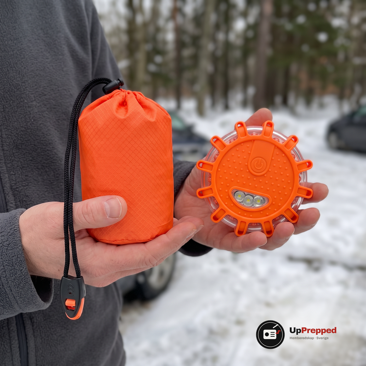 Man håller en orange nödsovsäck i ena handen och ett orange LED varningsljus i den andra för att visa hur små delarna är