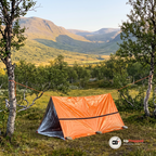 Orange nödtält upphängt med rep mellan två fjällbjörkar i fjällmiljö en klar sensommardag