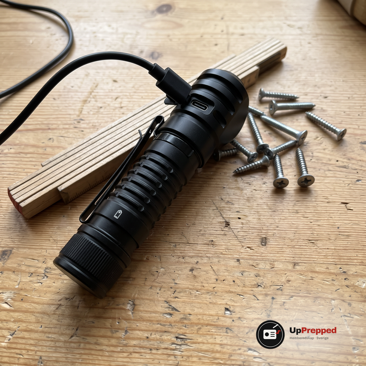 Pannlampan med fickclips liggande på en arbetsbänk i ett garage med en svart USB-C-kabel inkopplad i laddporten på lamphuvudet