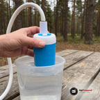 Hand håller den blå och vita pumpen ovanför en genomskinlig hink med vatten på ett picknickbord