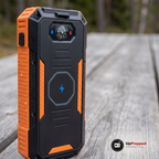 Närbild på powerbankens baksida med kompassfönster med blå och röd prick, rund Qi-yta med blixtsymbol och orange gummigrepp på ett grått plankbord