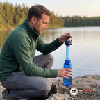 Man lyfter det svarta locket med filtret fastsatt ur den blå flaskan vid en sjö. Flaskan och locket ingår inte, bilden visar filtret i vår vattenflaska med inbyggt filter 650 ml