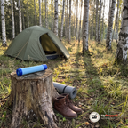 Reservfilter på en stubbe framför ett tält bredvid kängor och ett hoprullat liggunderlag i björkskog