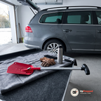 Utdragen teleskopspade med rött blad på en grå filt i bagageutrymmet på en kombi bredvid arbetshandskar, termos och snöborste