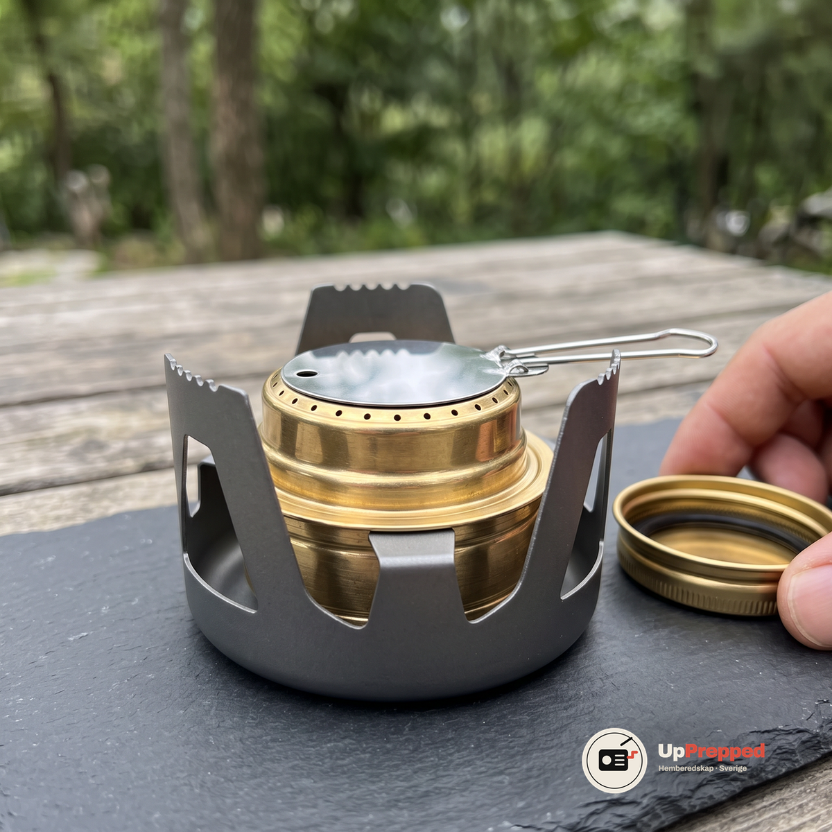 Närbild på plattan med trådhandtag på brännaren, med locket bredvid på ett skifferunderlag