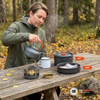 Person i olivgrön regnjacka häller vatten ur vattenkokaren i en emaljmugg vid ett picknickbord, med spritköket, kastrullen och stekpannan på bordet