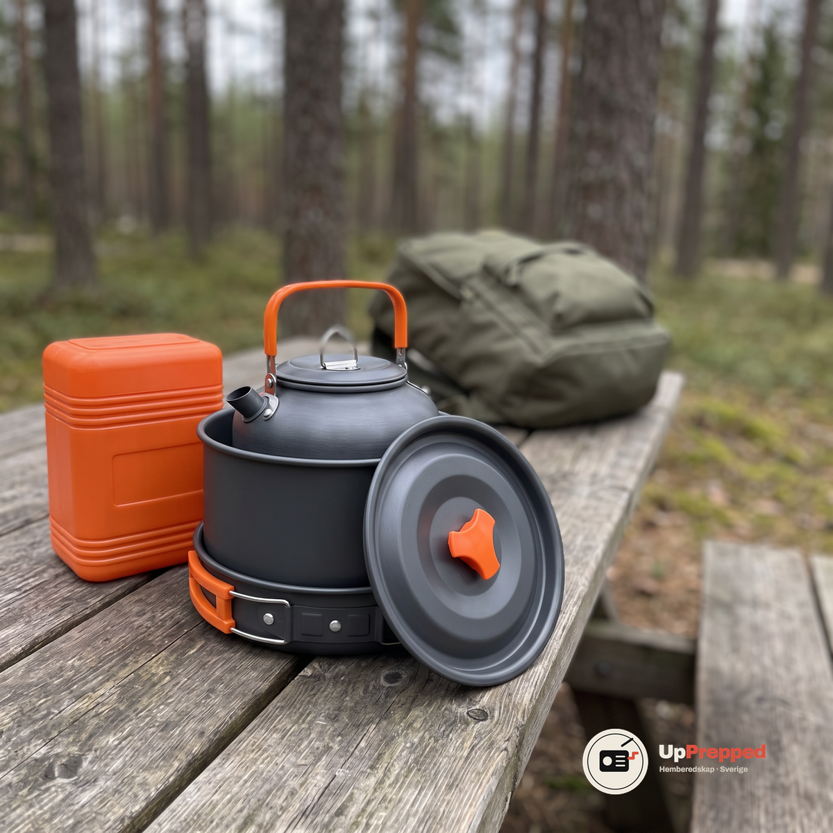Stekpanna, kastrull och vattenkokare staplade i varandra på en träbänk i skogen, med kastrullens lock lutat mot stapeln och en orange box bredvid