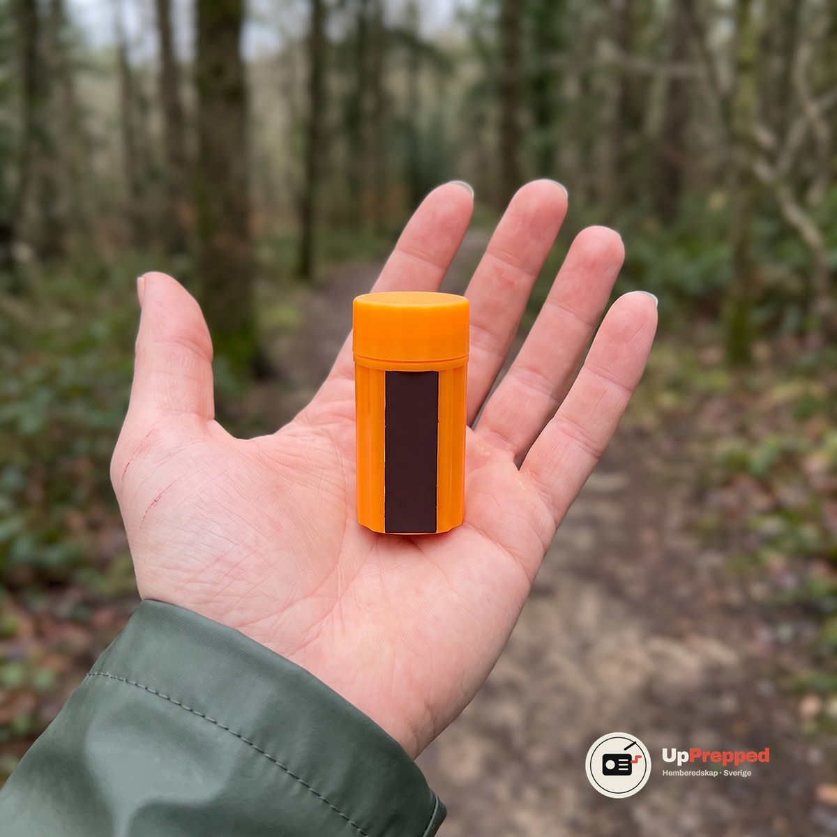 Öppen handflata med den orange behållaren med lock stående upprätt, som visar hur liten den är
